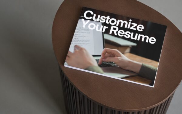 A brown table with a book on the top. The cover of the book shows hands working on a laptop. The book is called Customize Your Resume.